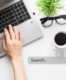 o persoana ce scrie la tastatura unui laptop langa o planta, o pereche de ochelari si o cana de cafea